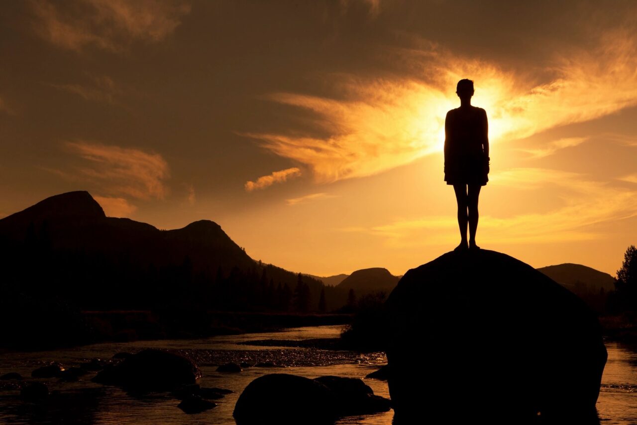 A person standing on a rock while watching the sun